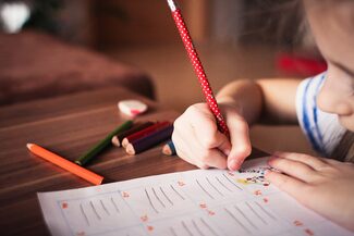 Ein Kind sitzt am Tisch und schreibt etwas in ein Schulheft.
