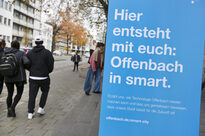 Menschen laufen an dem Plakat "Hier entsteht mit euch: Offenbach in smart."