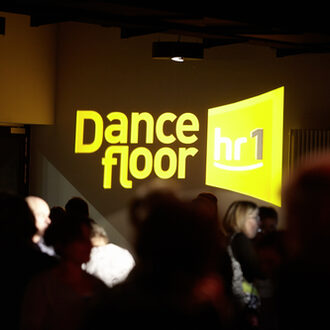 Gelbes Logo des Dancefloors und tanzende Menschen.