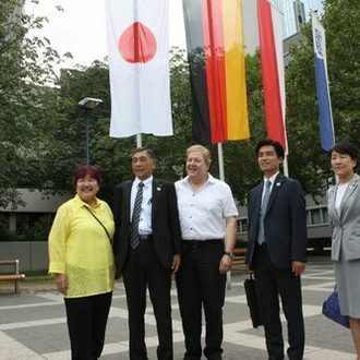 Mitglieder der japanischen Delegation vor den Fahnen am Rathaus.