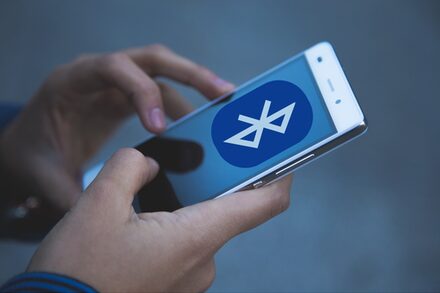 Hände halten ein Smartphone; auf dem Bildschirm ist das Bluetooth-Symbol zu sehen