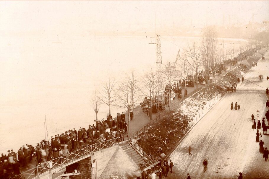 Menschen stehen 1909 auf einem Damm und beobachten das Mainhochwasser.