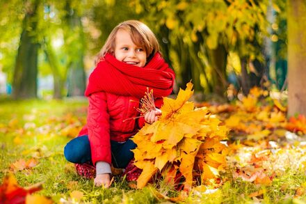 Kind mit roter Kacke sitzt auf Gras und sammelt buntes Laub