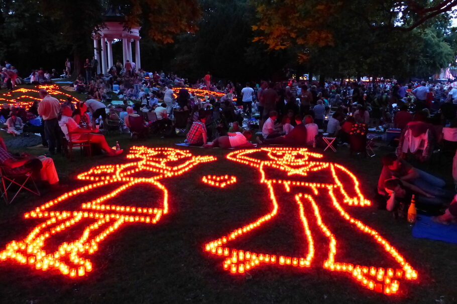 Menschen sitzen abends im Büsingpark neben Kerzen, die zu Motiven angeordnet sind.
