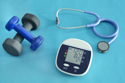 Hanteln, ein Stethoskop und ein Blutdruckmessgerät liegen auf einem Tisch.