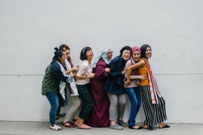 Sieben Frauen aus unterschiedlichen Kulturen stehen hintereinander und lachen.