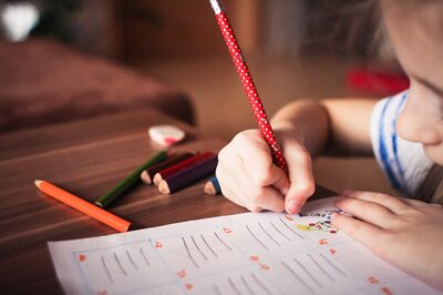 Ein Kind sitzt am Tisch und schreibt etwas in ein Schulheft.
