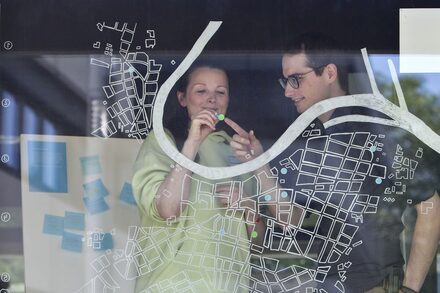 Schaufenster mit einem aufgemalten Stadtplan, dahinter stehen zwei Personen.