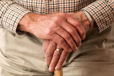 Zwei Hände eines älteren Mannes liegen auf einem Geh-Stock.
