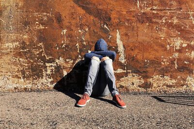 Ein junger Mensch sitz an einer Mauer und hat den Kopf traurig auf die Knie gelegt.