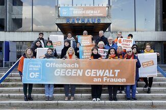 Personen stehen am Rathaus und halten ein Banner "Offenbach gegen Gewalt an Frauen"