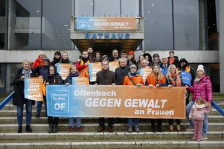 Gruppenbild vor dem Rathaus, die Personen auf dem Bild halten ein Transparent und Plakate in den Händen mit der Aufschrift "Offenbach gegen Gewalt an Frauen".