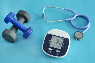 Hanteln, Blutdruckmessgerät und Stethoskop auf einer blauen Unterlage.
