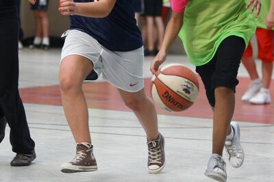 Kinder spielen in einer Turnhalle Basketball.