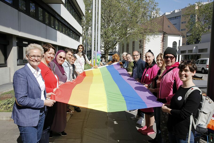 Die Bürgermeisterin hält mit anderen Personen die Regenbogenfahne.