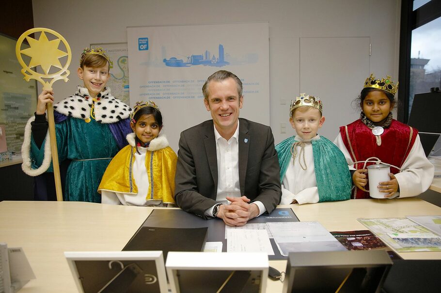 Der Oberbürgermeister sitzt am Schreibtisch, neben ihn vier Kinder, die als Sternsinger verkleidet sind.