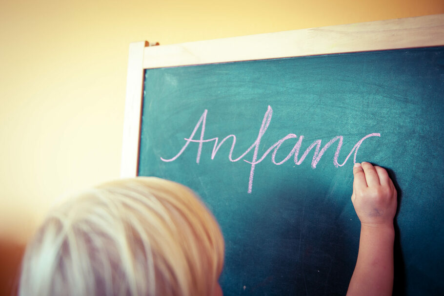Ein Kind schreibt das Wort "Anfang" auf eine Tafel
