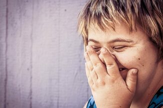 Das Foto zeigt ein lachendes Mädchen mit Trichosomie 21.