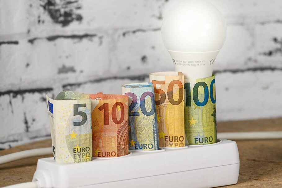 Das Foto zeigt eine Steckdose, in der Geldscheine stecken und eine Glühbirne.