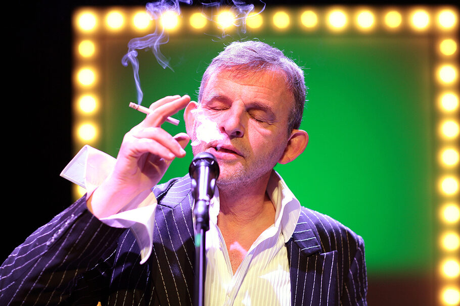 Der Schauspieler Dominique Horwitz raucht Zigarette und singt in ein Mikro.