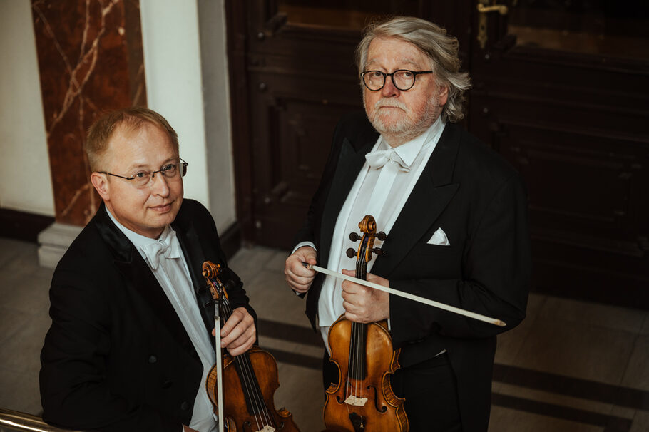Die beiden Musiker des Duos halten ihre Geigen in der Hand.
