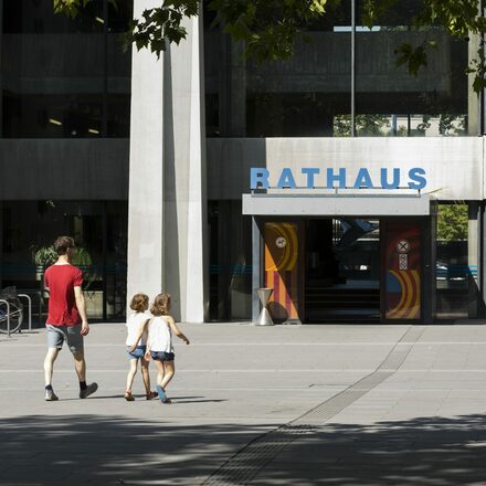 Ein Mann geht mit zwei Kindern zum Eingang des Rathauses in Offenbach.