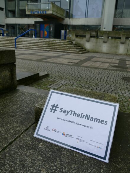 Ein Schild mit der Aufschrift "say their Names" vor dem Rathaus