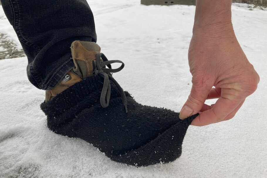 Auf dem Foto sind Schuhe auf Schnee zu sehen, über die ein Socken gezogen ist.