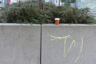 Ein Kaffeebecher To Go steht auf einer Mauer, die mit Farbe beschmiert ist.