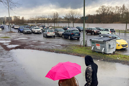 Ein Paar mit Regenschirm geht über den Mainuferparkplatz.