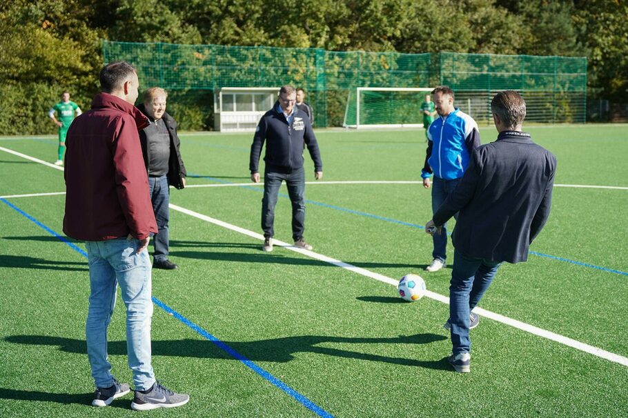 Fünf Männer spielen auf einem Sportplatz Fußball.