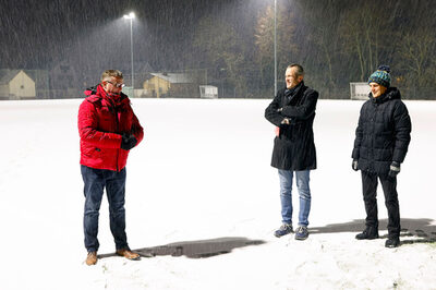 Drei Männer stehen auf einem verschneiten Fußballplatz.