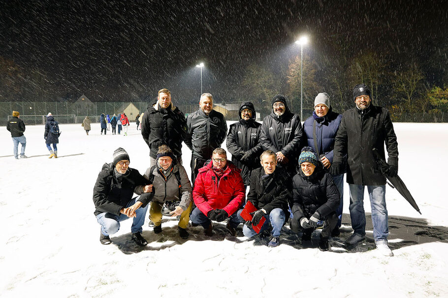 Eine Gruppe von Männern hat sich auf einem verschneiten Fußballplatz zum Gruppenfoto aufgestellt.
