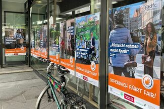 Plakate hängen in einem Schaufenster, davor steht ein Fahrrad.