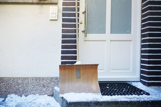 Eine Schneeschippe steht vor einem verschneiten Hauseingang.