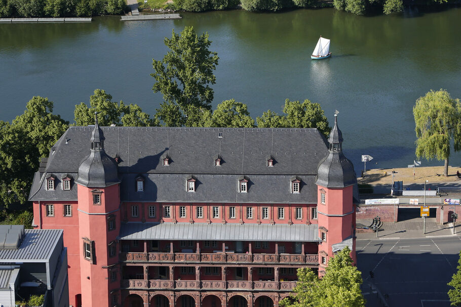 Blick auf das Isenburger Schloss aus der Vogelperspektive, im Hintergrund der Main, auf dem ein Segelboot fährt.