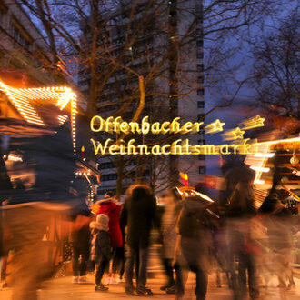 Menschen laufen abends über den erleuchteten Offenbacher Weihnachtsmarkt.