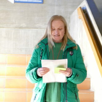 Eine blonde Fraue mit grüner Jacke hält Zettel in der Hand und hält eine Rede