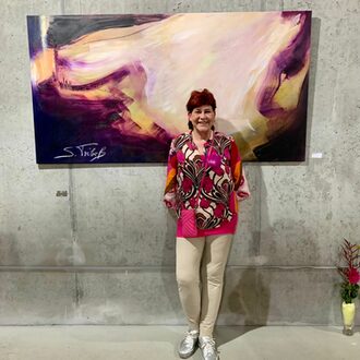 Eine Künstlerin steht vor einer grauen Wand und einem Bild.