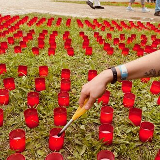 Eine Hand mit einem Feuerzeug zündet rote Kerzen an.