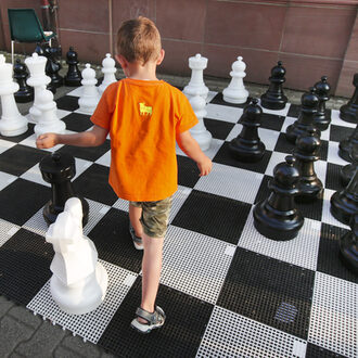 Ein Kind geht über ein Schachfeld mit großen Schachfiguren.