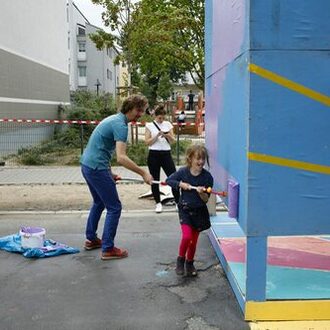 Mann und Kind streichen eine Spielwand.