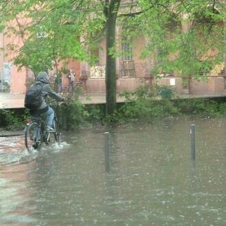 Fahrradfahrer fährt durch Wasser in Folge eines Starkregens