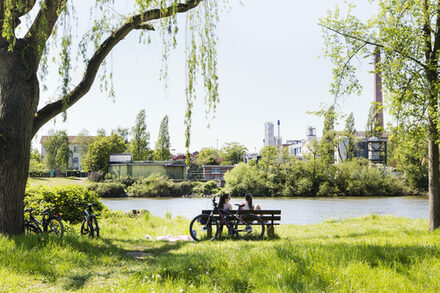 Zwei Radfahrerinnen sitzen auf einer Bank am Mainufer
