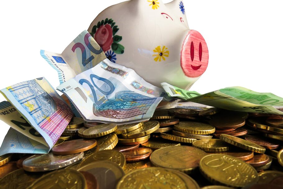 Symbolbild Haushalt: Geld türmt sich vor einem Sparschwein aus Porzellan.