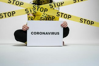 Frau mit Schild "Coronavirus" hinter Absperrbändern, auf denen Stop steht