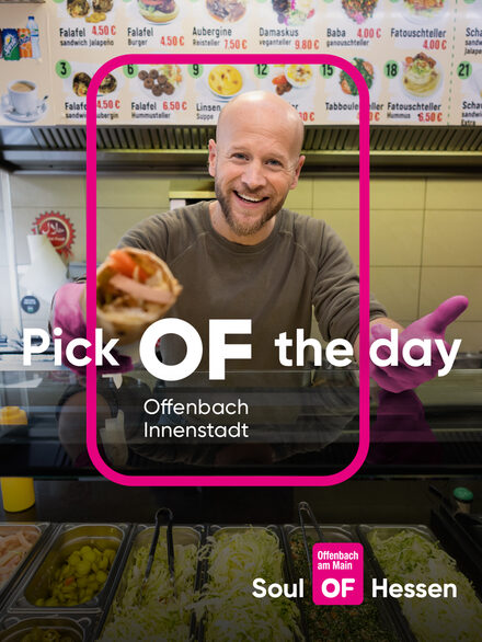 Ein Mann hinter einer Essenstheke und dem Offenbach-Logo mit dem Kampagnentitel in pinker Farbe.