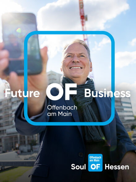 Ein Mann mit Anzug vor einem Gebäude und Baukränen. Er macht ein Selfie. Auf dem Bild liegt das Offenbach Logo sowie der Kampagnen-Slogan.