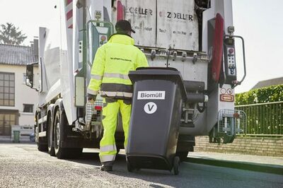 Ein Mitarbeiter der Stadtwerke bringt eine Biomülltonne zum Abfallwagen