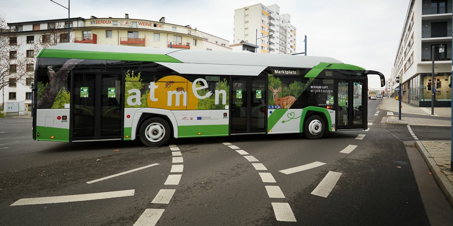 Ein grün-weißer E-Bus biegt um die Kurve.